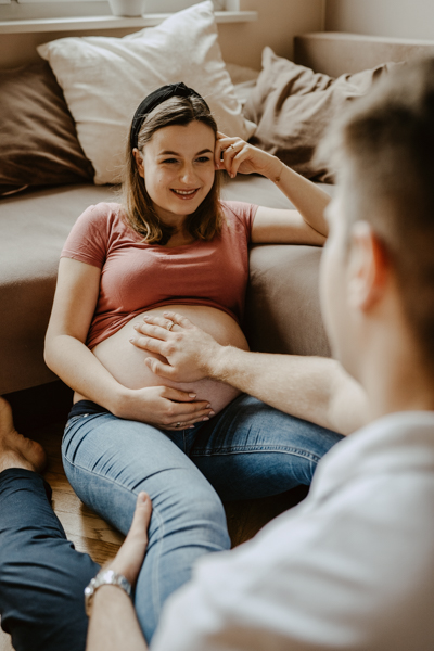 kobieta w ciąży uśmiechająca się do męża pozująca podczas sesji brzuszkowej
                                     
